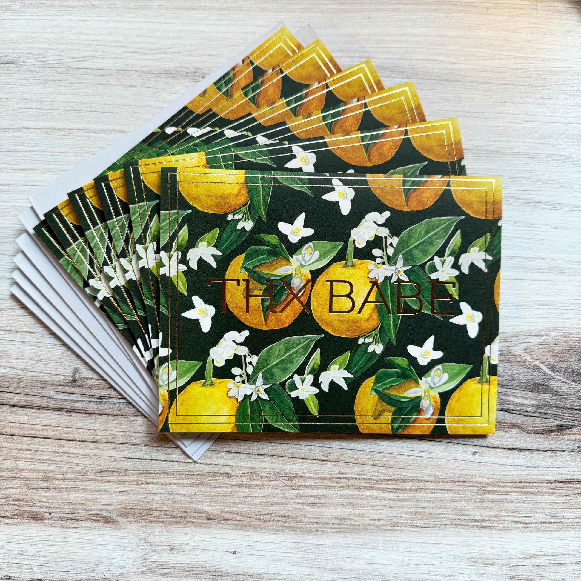 Set of 6 folded full color gold foil stamped cards with dark green background and watercolor painted orange blossom flowers and oranges in foreground, blank inside. 6 luxe gray envelopes.
