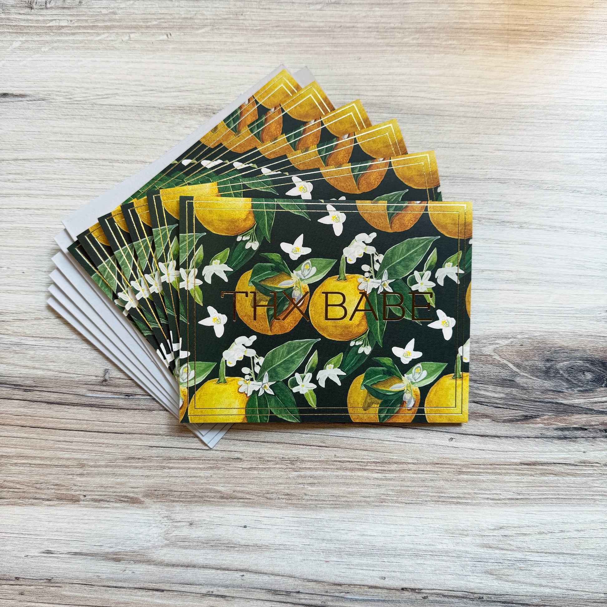 Set of 6 folded full color gold foil stamped cards with dark green background and watercolor painted orange blossom flowers and oranges in foreground, blank inside. 6 luxe gray envelopes.